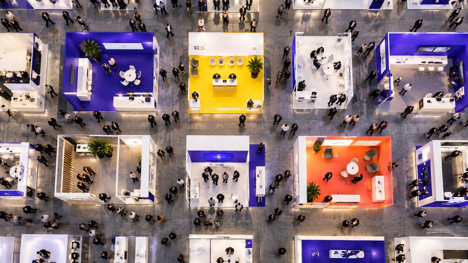 A busy exhibition hall seen from above, with booths, aisles and visitors.